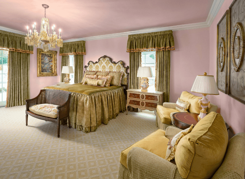 粉红色的主卧室里有土绿色的窗帘和床，扶手椅放在钻石图案的地毯上。