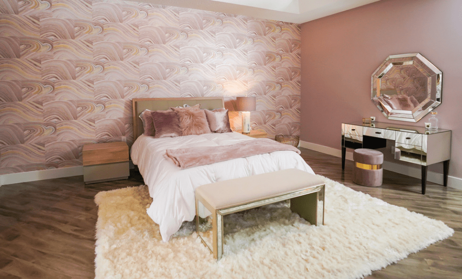 华丽的主卧室展示了一张白色的床和一张皮革长凳，放在有图案的墙壁上。它包括一个带有镜子的梳妆台，配有一面八角形镜子和一个灰红色的凳子。
