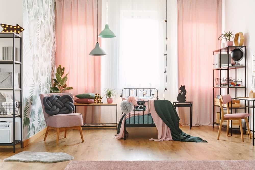 粉红色的卧室里有一张小金属床，与金属架子和桌子相辅相成。它有一个粉红色的木制软垫椅子，配有一个独特的灰色抱枕。