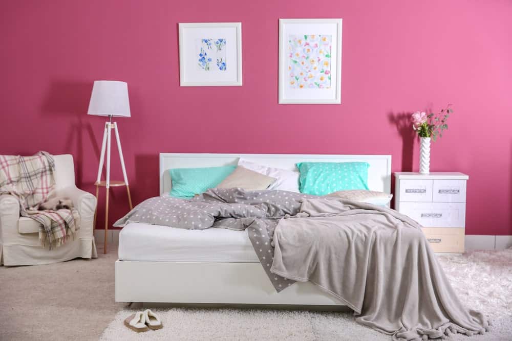 粉红色的主卧室，白色的床上有一对墙壁艺术框架，灰色的被子和毯子包裹着分层的地毯。