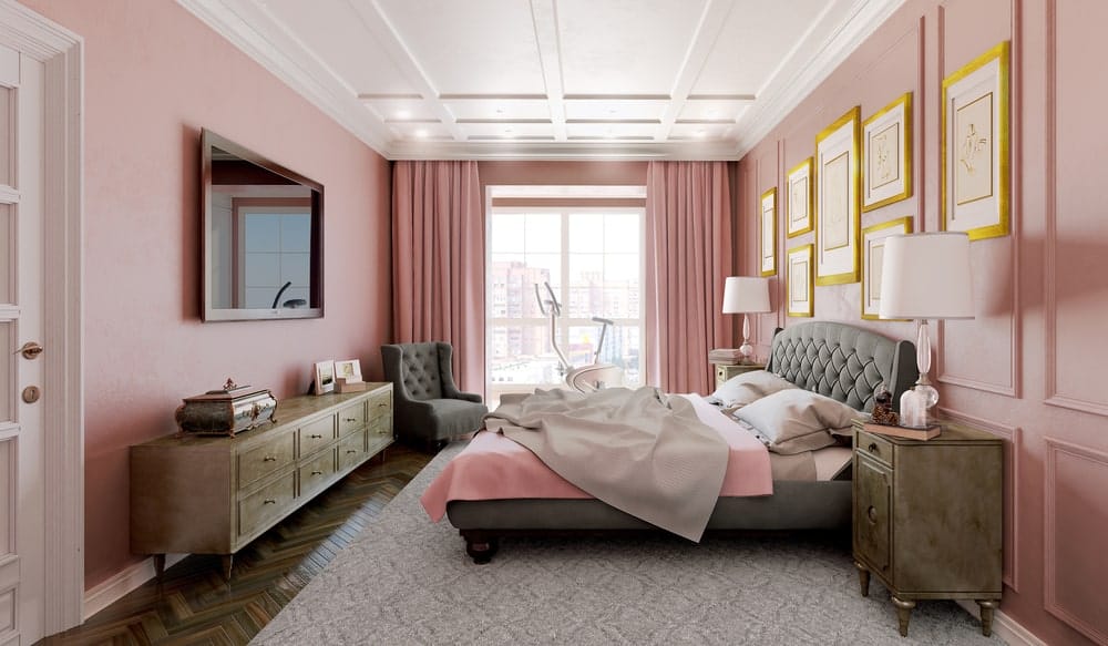 精致的主卧室拥有白色格子天花板和粉红色的全壁板强调墙，装饰着金色的画廊框架。