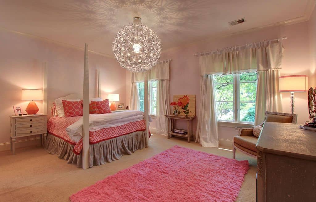 华丽的主卧室展示了一张四柱床，床上装饰着粉红色的床品，由可爱的球形吊灯照亮，自然光从窗户射进来。