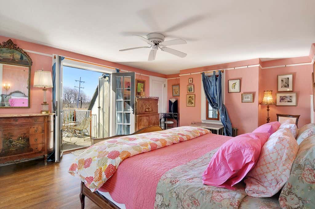 粉红色的主卧室，有一扇玻璃落地门，通往阳台。它包括一个木制床架和一个带有华丽镜子的木制抽屉。