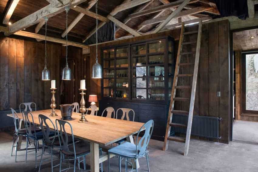 围绕着大木制餐桌的铁椅子色调柔和，与灰色的混凝土地板相映成辉，也与教堂天花板上木制横梁上悬挂的钟形吊灯相呼应。