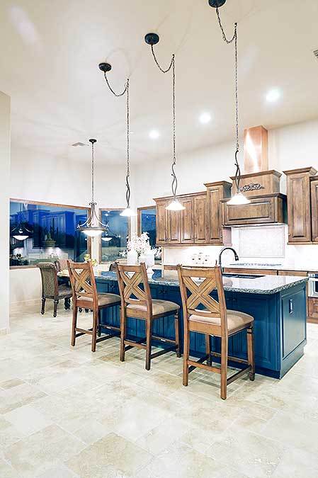 明亮的蓝色木制厨房岛在这个西南风格的厨房中脱颖而出，浅色的大理石地板与早餐吧台上的木椅相辅相成，由明亮的吊灯照亮。这也照亮了半岛的木制摇床橱柜。
