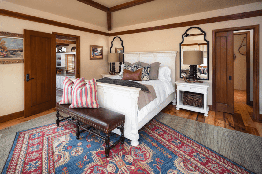 一个舒适的西班牙卧室，特色图案超过印花设计。这一点在纯灰色地毯上的彩色图案地毯上得到了强调，甚至在纯白色床上的图案枕头也与两个白色床头柜相匹配。两盏床头灯后面可爱的一面镜子使这个房间更加复杂。