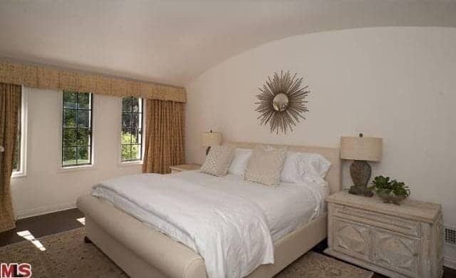 简单的主卧室有一个冰屋拱形天花板，主要是白色的。边桌、灯和床架的米色给房间带来了一种温暖的中性感觉。房间里最引人注目的细节是板头的壁挂式黄金艺术，类似于太阳或十字架。
