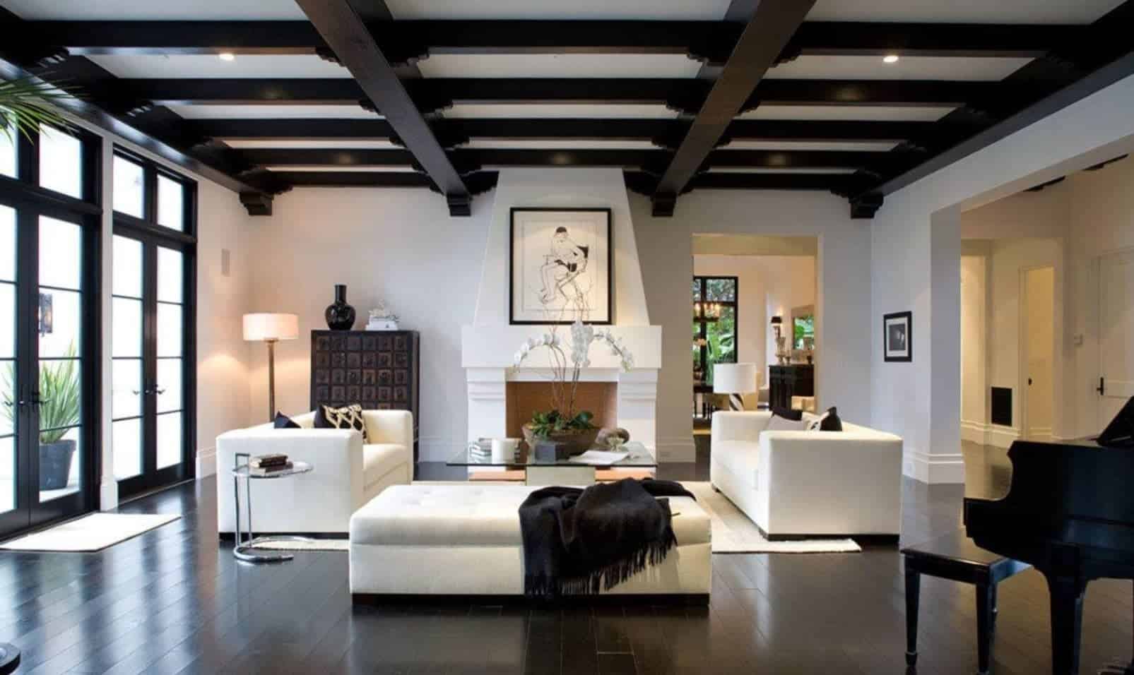 现代的白色客厅与时尚的黑色横梁天花板和硬木地板形成了美丽的对比。它有白色的沙发和簇绒长椅，配以黑色的枕头和毯子。