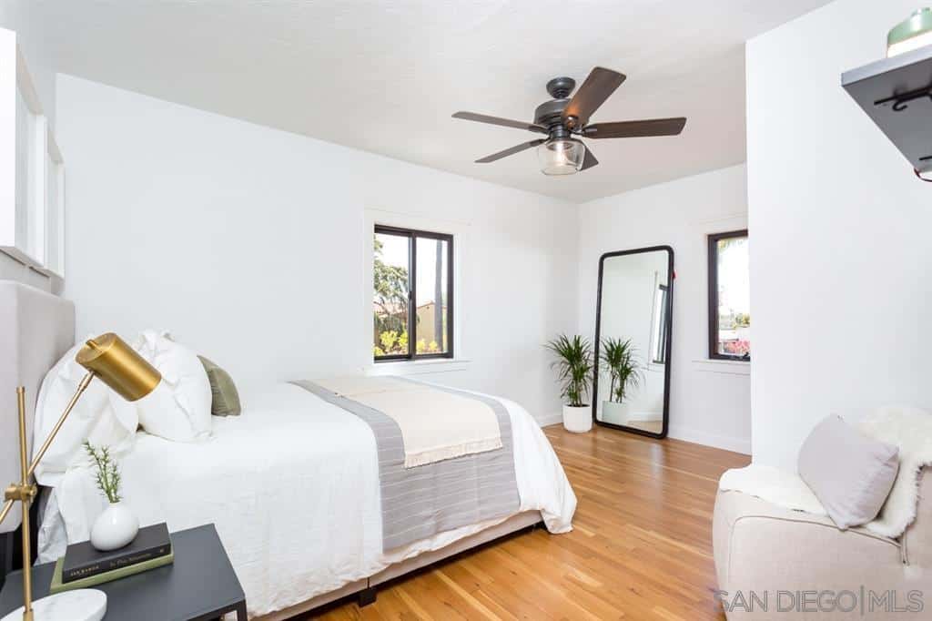 一个以白色和灰色为主色调的简单而温馨的卧室。这强调了地板和天花板上安装有内置灯具的木制棕色细节。边桌上的绿色植物和金色黄铜灯的小细节为房间增添了个性。