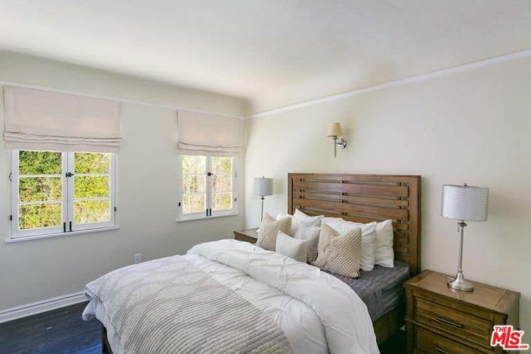 木质板条床头板与这间西班牙式卧室的白墙相映成色。它在风格和材料上完美地连接了两个床边抽屉。床两侧的一对银色台灯为房间增添了一抹金属色，与床头板上方的壁挂灯相得益彰。