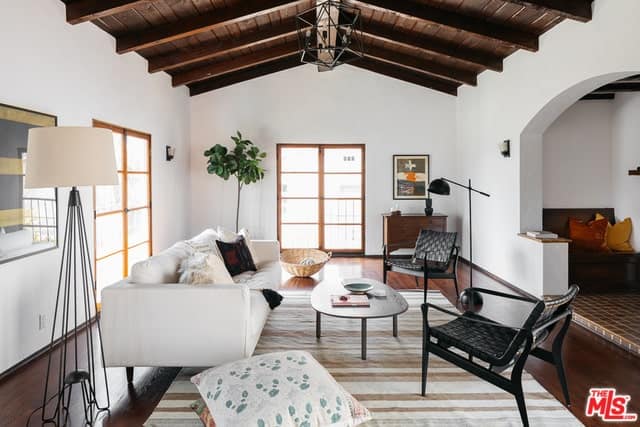 舒适的客厅，木梁天花板和硬木地板，上面有米色条纹地毯。房间里有一张白色沙发，配上一张木制咖啡桌和几把黑色椅子。