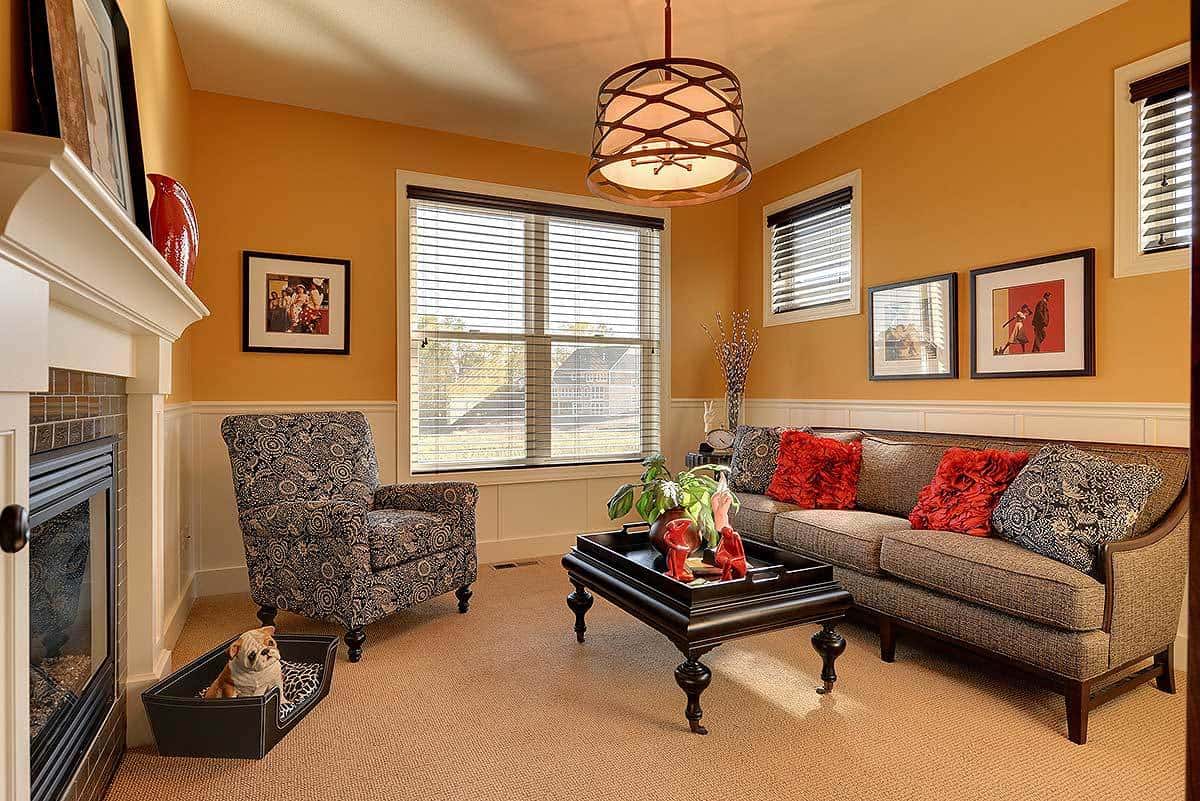 这是一间温馨的客厅，土黄色的墙壁与护墙板相得益彰。深灰色的花纹沙发套装和黑色木制咖啡桌与米色地毯地板相映成趣。