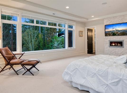 这是一间宽敞的卧室，米黄色的地毯地板与墙壁和天花板相匹配。床对面的大玻璃窗是一个舒适的休息区。