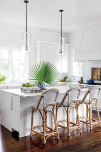 这个舒适的白色厨房搭配蓝色和自然元素，营造出轻松的海滩氛围。深色木地板与全白色的摇床柜和白色镶板天花板形成了鲜明的对比。