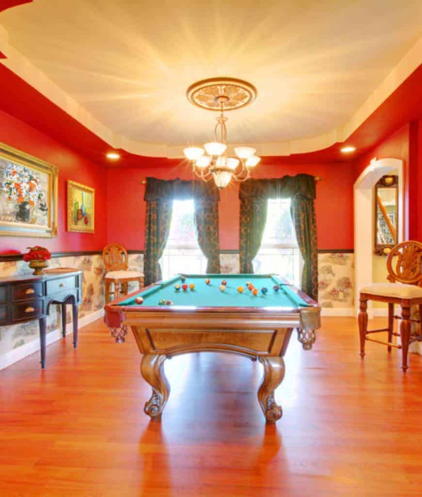 在这个红色的经典房间里，一张爪形台球桌是最引人注目的地方，天花板上悬挂着一盏枝形吊灯。它配有深色木控制台桌子和硬木地板上的圆形靠背椅。