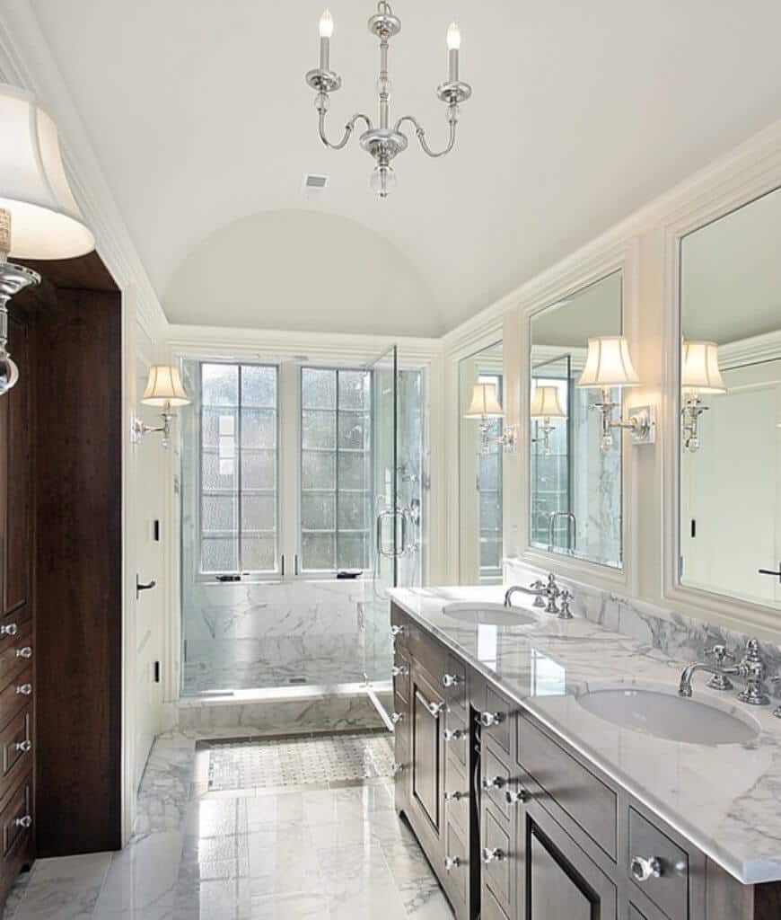 这间主浴室设有步入式淋浴间和双水槽梳妆台，带有装有玻璃旋钮的深色木橱柜。它有一个大理石台面，与地板和墙壁相匹配，形成一种有凝聚力的外观。