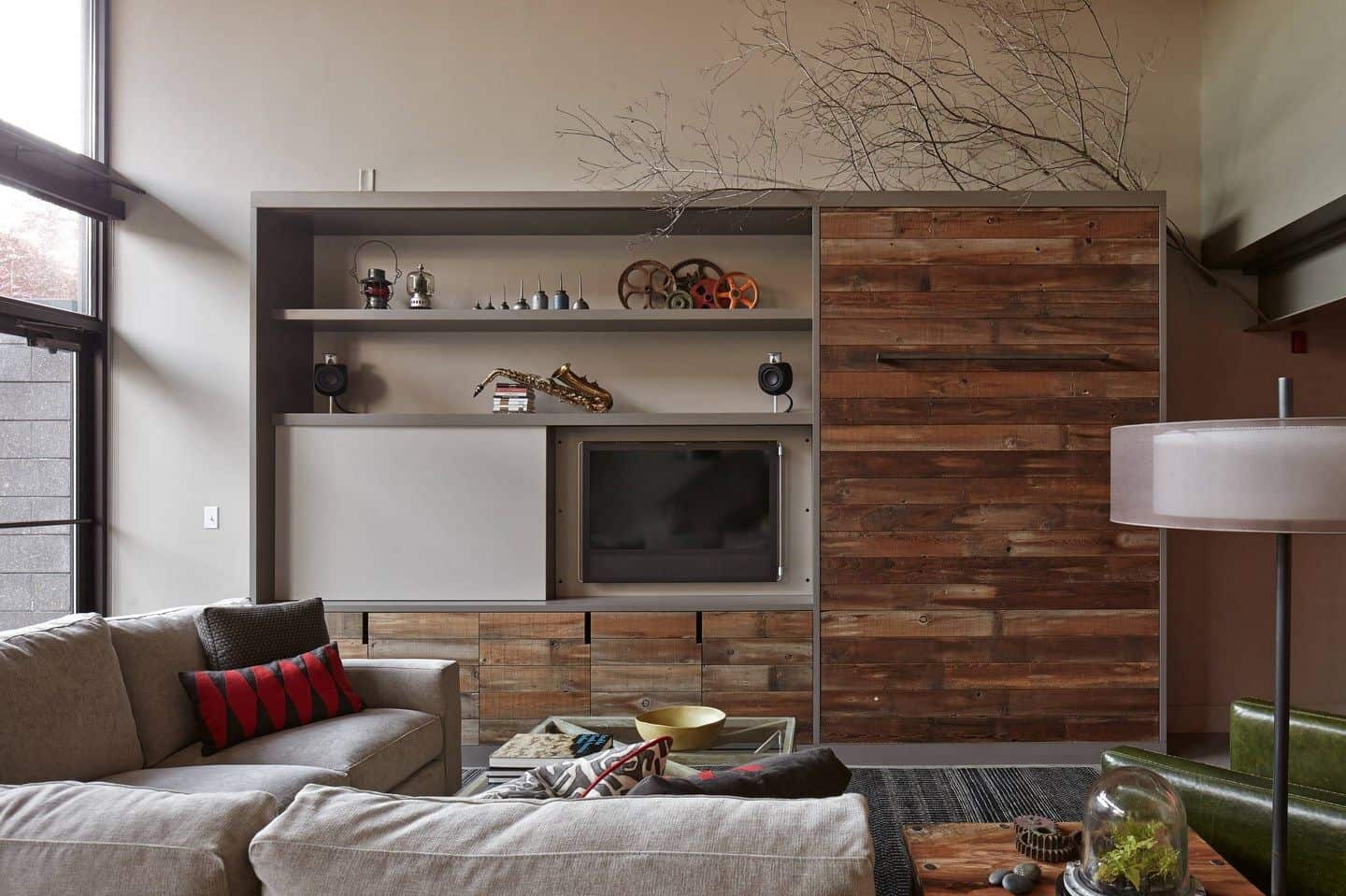 这间客厅有一面木镶板墙，配有开放式书架和电视。它有一个l形的组合家具，还有一张放在灰色地毯上的玻璃面咖啡桌。