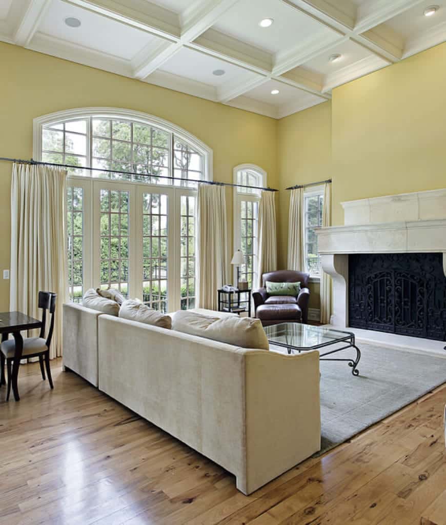 黄色的客厅里有一张灰色沙发和玻璃面咖啡桌，正对着大理石壁炉，壁炉被华丽的锻铁栅栏包裹着。