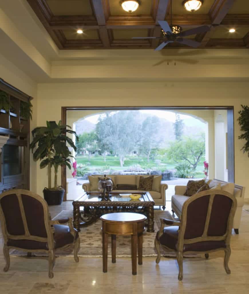 热带客厅，拥有可爱的绿色室外景观，大理石地板和固定有平装和嵌入式灯的方格天花板。
