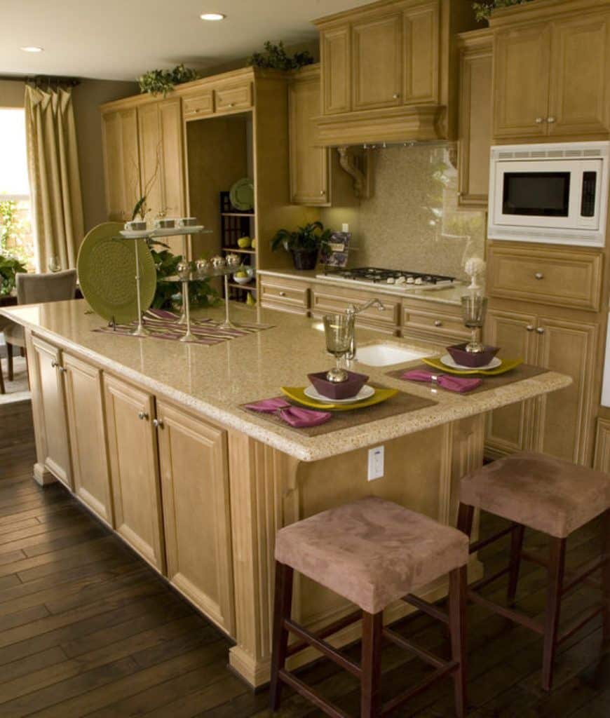 全木厨房提供白色微波炉和厨房岛，顶部是米色大理石柜台，搭配棕色天鹅绒吧台凳。