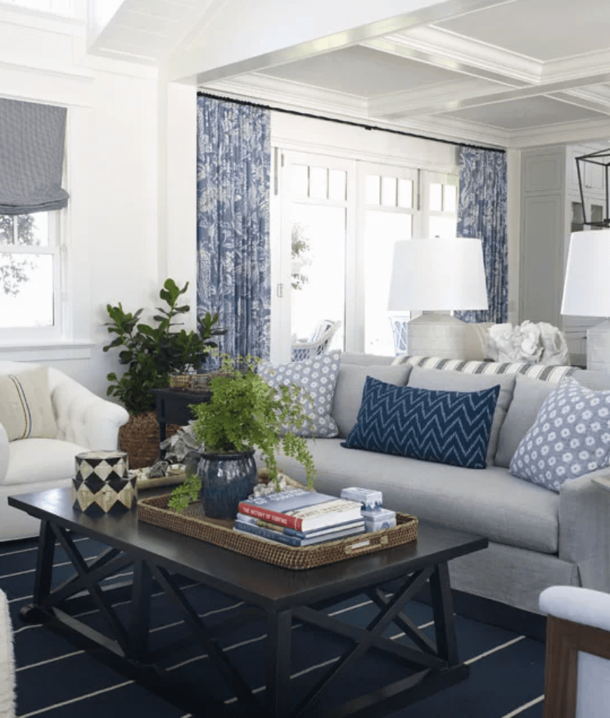 清新的客厅里有一张灰色沙发，上面装饰着碎花和chevron枕头，还有一张黑色咖啡桌，放在深蓝色条纹地毯上。