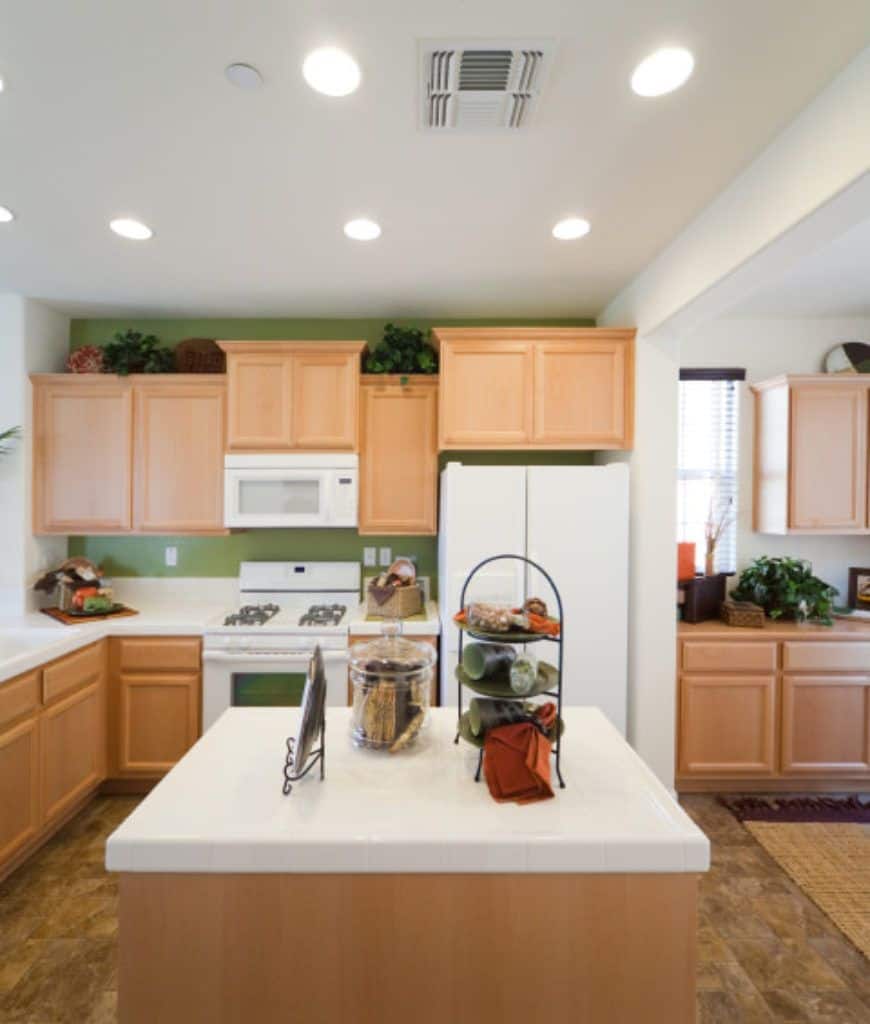 一个迷人的厨房，光滑的木制橱柜和白色电器固定在苔藓绿色的墙壁上。它包括一个中央厨房岛台，顶部有一个玻璃罐和金属架。