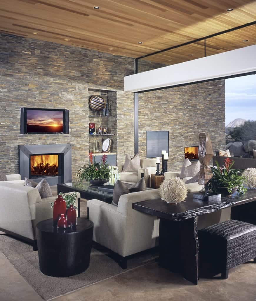 现代风格的客厅以石砖墙为特色，配有电视、金属壁炉和摆满各种装饰品的嵌入式架子。