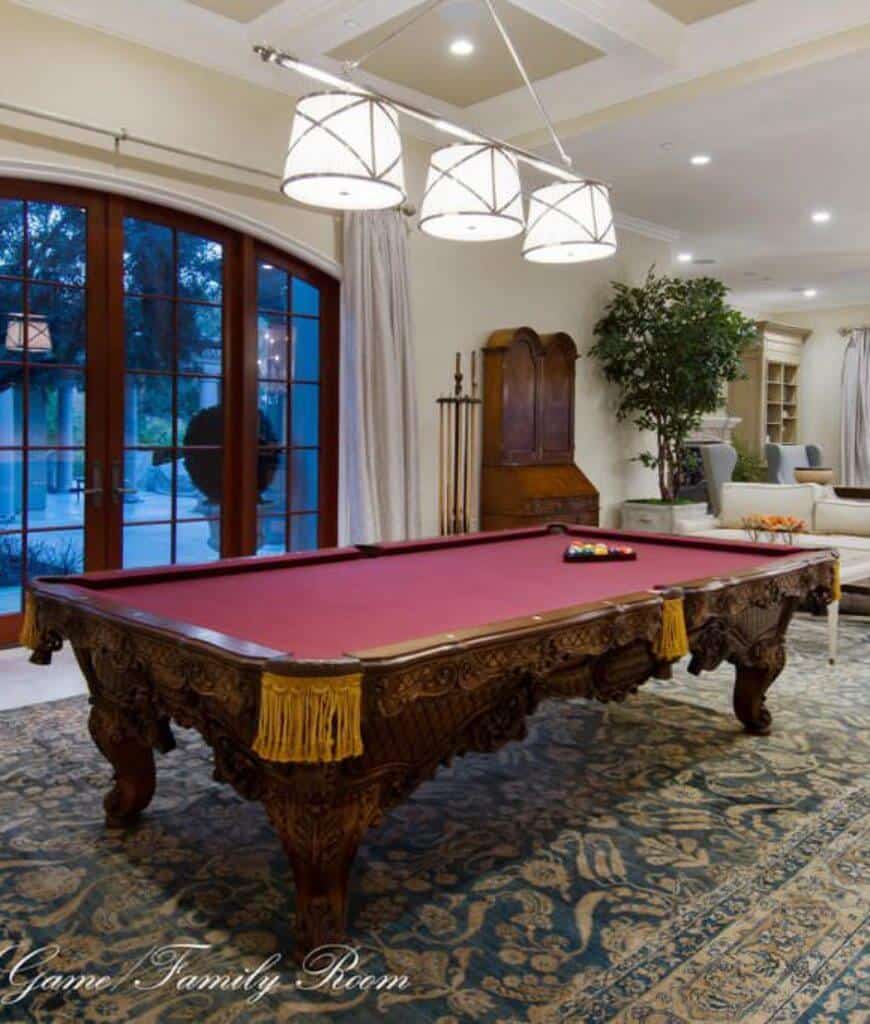 传统的家庭娱乐室展示了一张雕刻的木制台球桌，它坐落在经典的区域地毯上，格子天花板上悬挂着鼓形吊坠。
