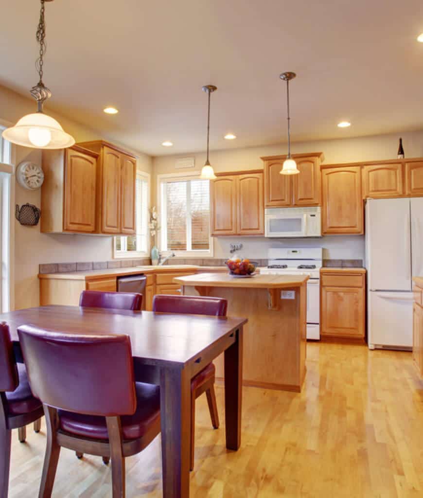 温暖的厨房展示了白色的电器和光滑的木制橱柜，与厨房岛相匹配。深色木质餐桌旁的梅色椅子更突出了这一特色。