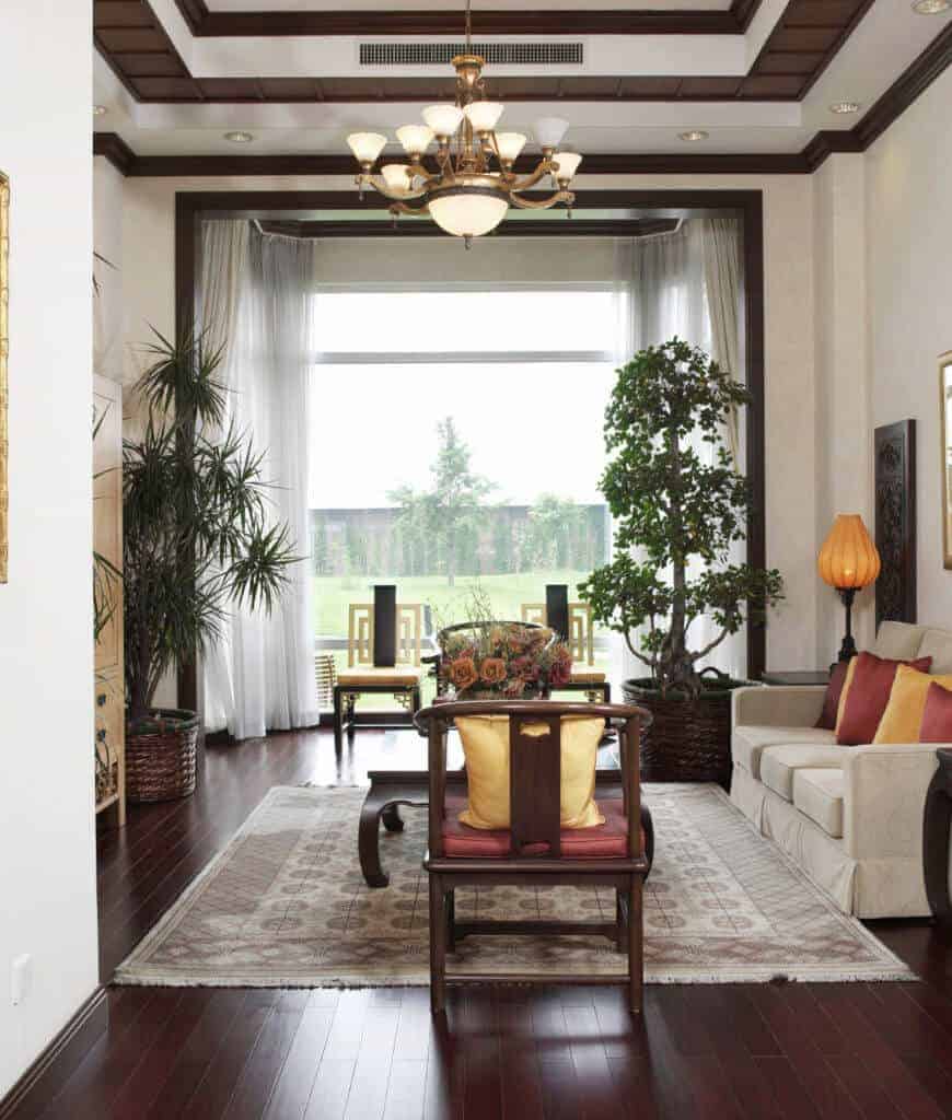 清新的客厅拥有木制扶手椅和灰色的部分，强调红色和黄色相间的枕头。它有木板地板和通高的玻璃，可以俯瞰郁郁葱葱的绿色植物。