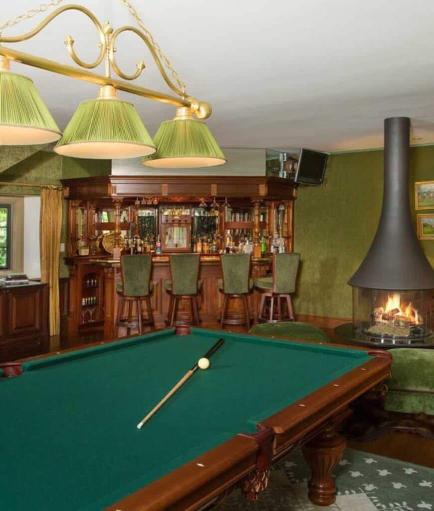 绿色男人洞在角落酒吧区旁边设有一座独立壁炉，旁边还有一张台球桌，台球桌放在有图案的地毯上，由黄铜挂件照亮。