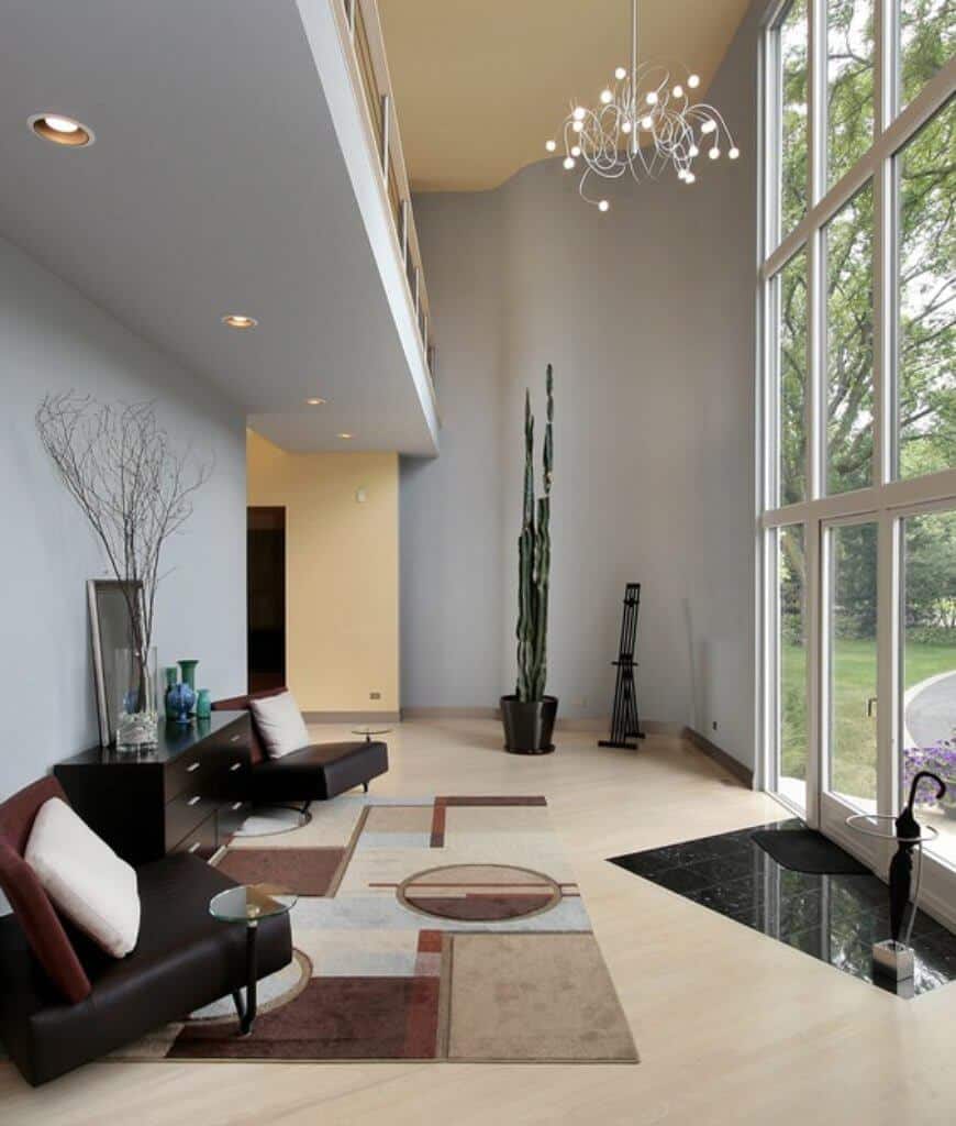 现代客厅，浅色硬木地板和全高玻璃，带来充足的自然光线。它包括一个独特的枝形吊灯和黑色的木控制台桌子，中间是黑色的皮椅子，上面铺着醒目的地毯。