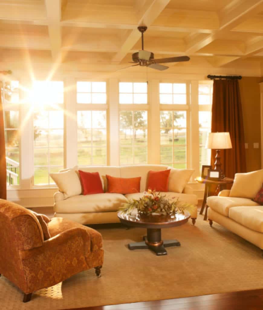 明亮的客厅里摆放着棕色扶手椅和圆形咖啡桌，咖啡桌放在天鹅绒地毯上，白色沙发上点缀着橙色的枕头。