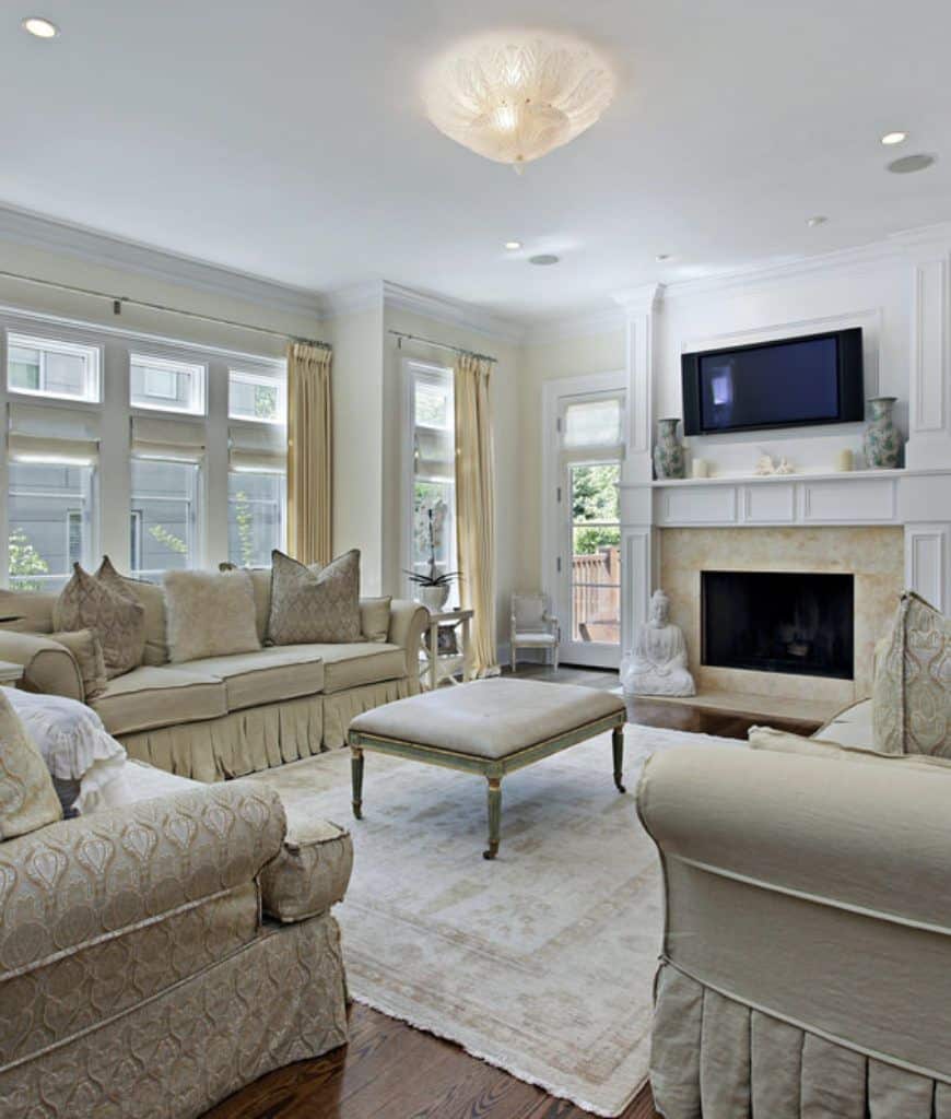 优雅的客厅设有一个皮革脚凳，坐在一个区域地毯周围米色部分。它包括一台安装在壁炉上方的电视，以一座白色雕塑为特色。