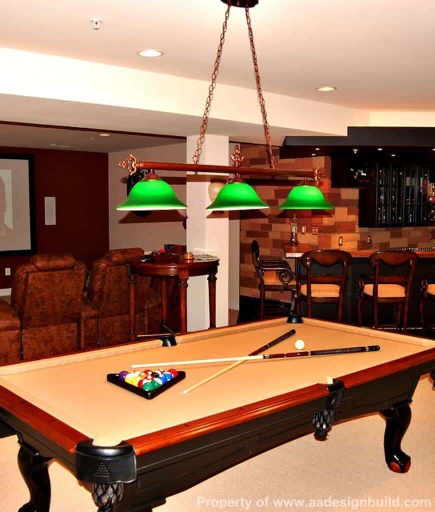 在这个娱乐室里，绿色的吊灯非常显眼，里面有吧台和台球桌，位于皮质组合家具和圆形木桌的后面。