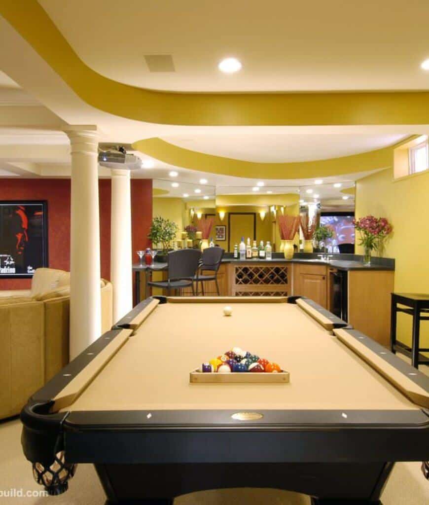 豪华娱乐室，客厅紧挨着弯曲的酒吧区，面对着白色圆柱排列的黄色台球桌。
