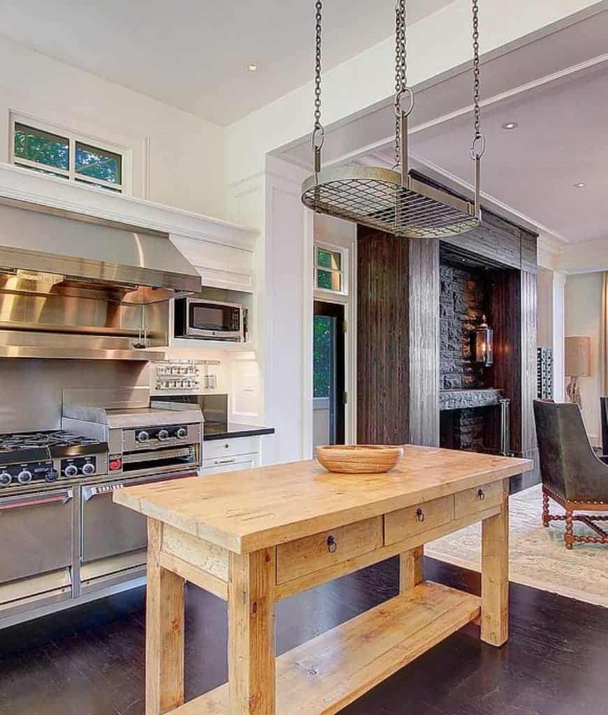 厨房里有一个椭圆形的锅架，放在天然木质早餐桌上，餐桌上有一个木碗，厨房里有白色的橱柜和不锈钢用具。