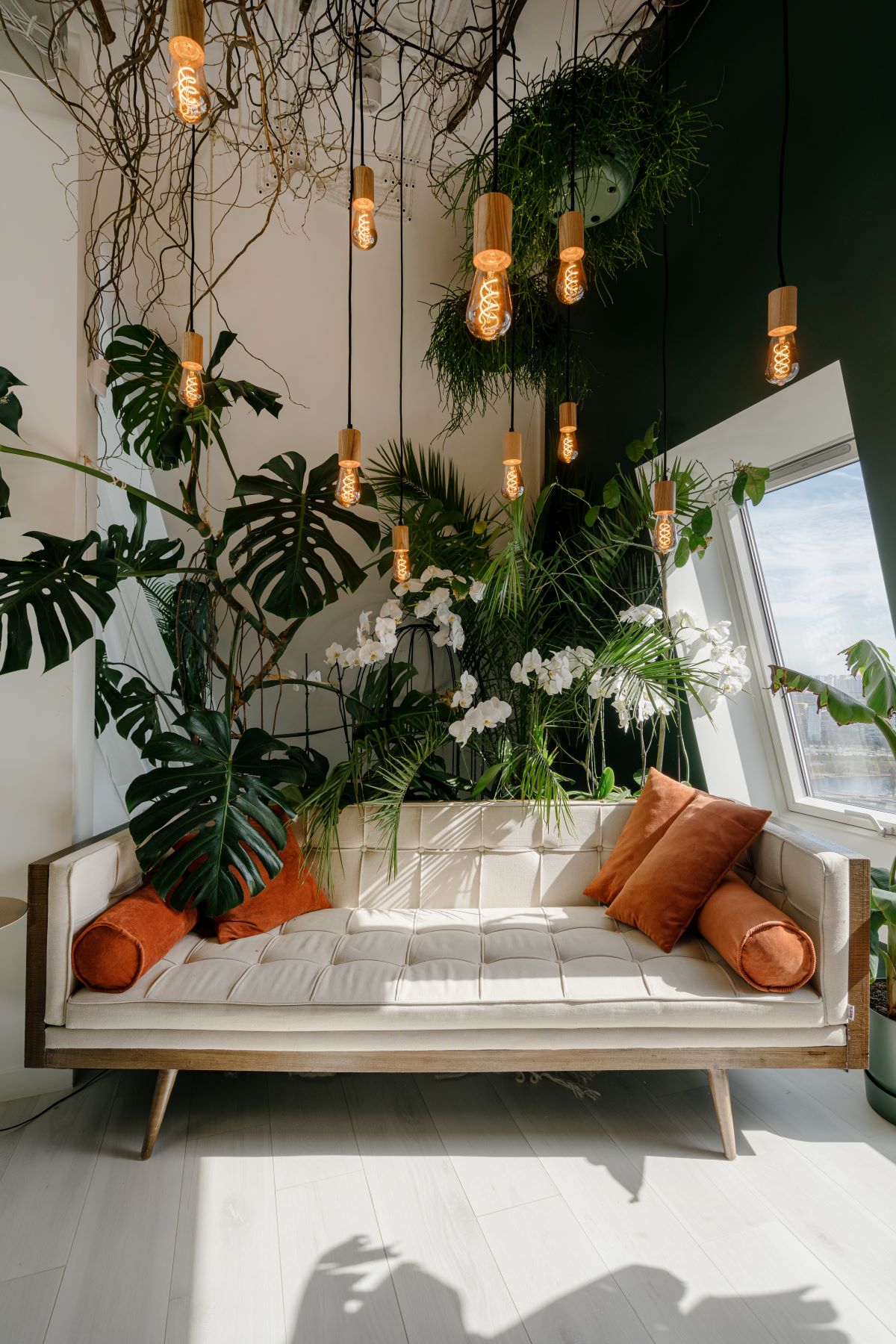 热带boho-style客厅特征与橙色本世纪中叶现代米色沙发枕头和一个大窗口带来充足的自然光照。plant-filled空间还宽,光硬木木板地板和吊坠照明。