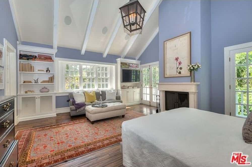 宽敞的主卧室有白色的床，灰色的沙发和壁炉，周围有蓝色的墙壁和硬木地板。