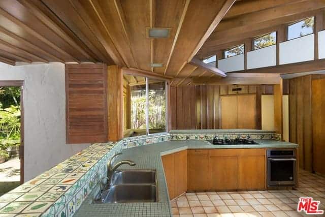 大厨房有一个j形的厨房半岛，厨房台面上装饰着灰色的小瓷砖，后挡板上的彩色瓷砖更增强了它的效果，后挡板上有各种各样的图像。这个设置由天花板、窗户、橱柜和墙壁的木质元素构成。