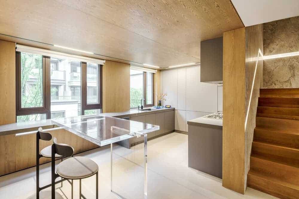 这个简单而小的厨房就在木楼梯下面。这与厨房的木墙和天花板相匹配。明亮的白色地板增强了这一点，水池区域的窗户上的自然光使地板变得明亮。