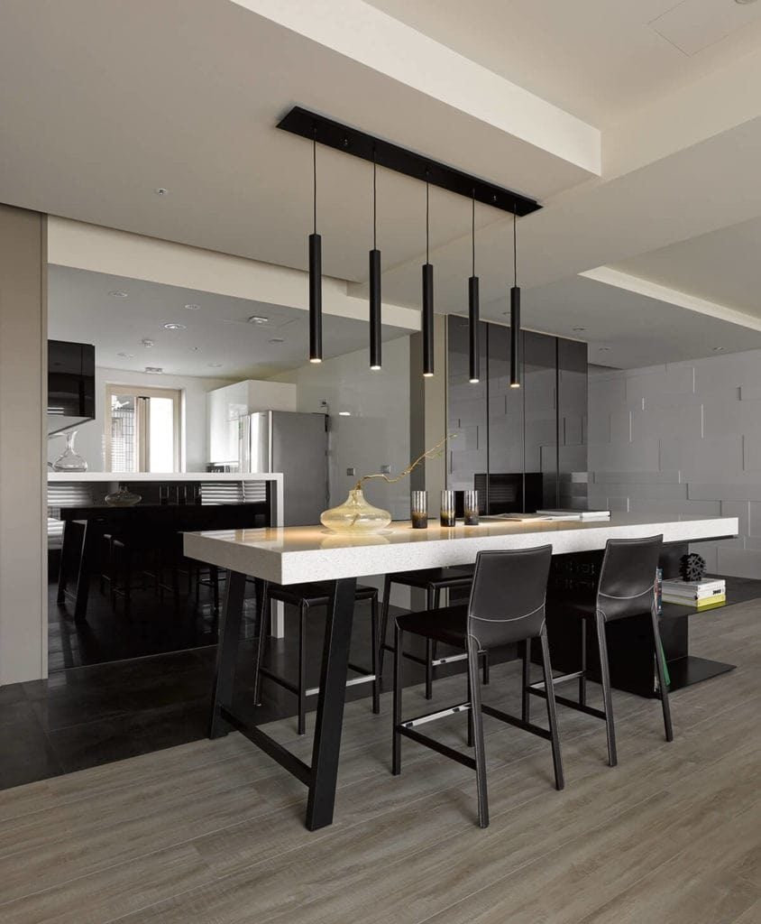 优雅纤细的黑色吊灯悬挂在厨房岛的白色台面上，与厨房半岛形成对比，白色台面采用瀑布式装饰和设计。这些都与地板的黑色瓷砖相辅相成。
