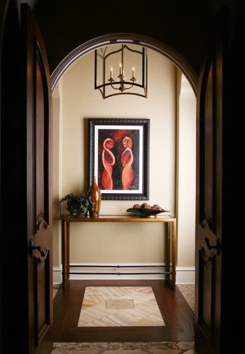 深色木质拱形门通往米色门厅，门厅展示了有趣的墙壁艺术和由笼状吊坠照亮的木质控制台桌子。