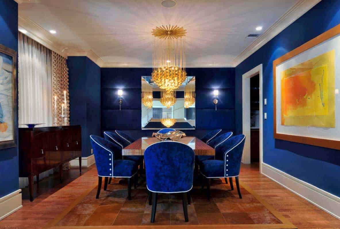 优雅的餐厅设置，蓝色的座椅与蓝色的墙壁相匹配。房间里有一盏迷人的枝形吊灯。