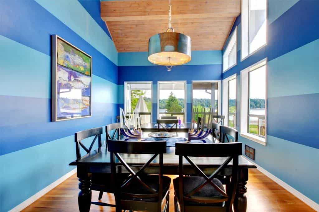 一间蓝色的餐厅，有两套餐桌。房间有高高的天花板和玻璃窗，可以俯瞰宁静的环境。