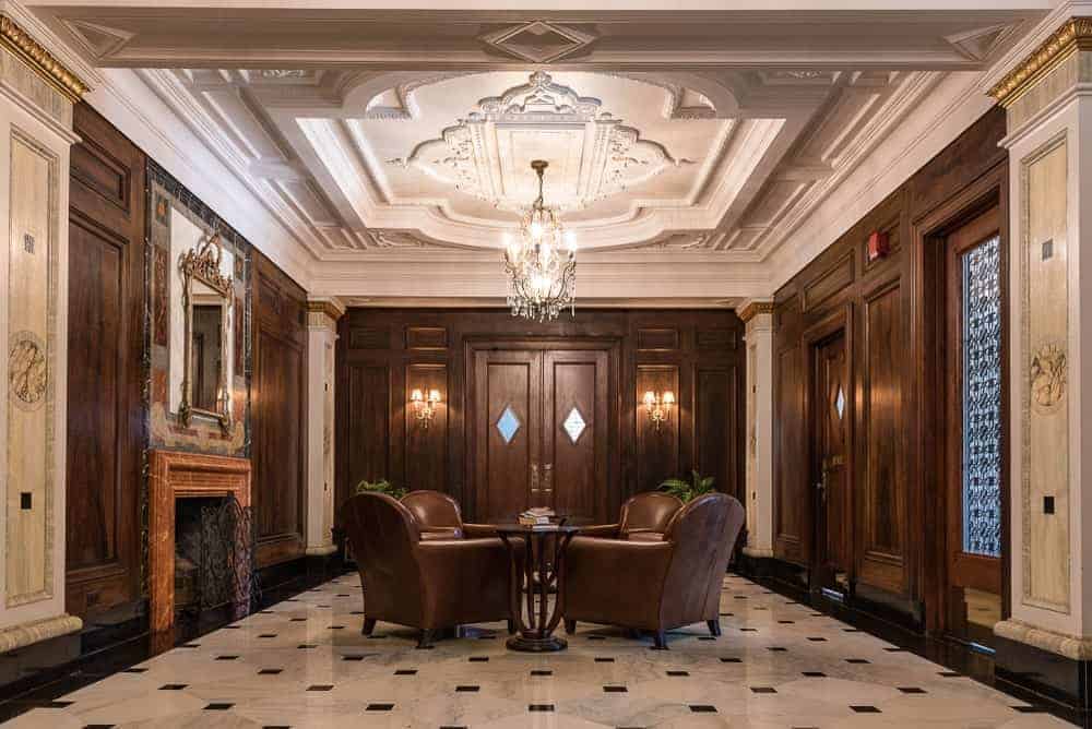 一个令人惊叹的棕色门厅，提供一个圆桌，漂亮的椅子设置在优雅的瓷砖地板上，由一个华丽的吊灯悬挂在装饰的天花板上照明。