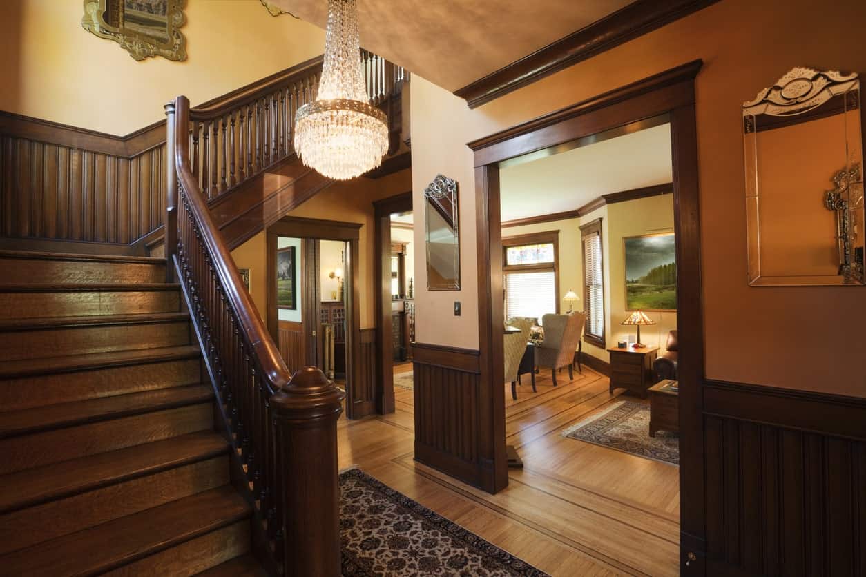 这是一个优雅的棕色门厅，以深色木质装饰的墙壁为主导，与木地板相辅相成，木地板顶部有深色图案的区域地毯。浅棕色的天花板上挂着一盏优雅的小水晶吊灯。