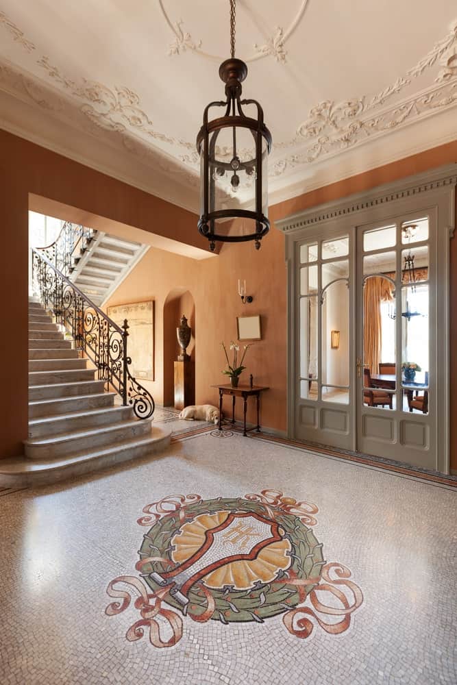 宽阔门厅的土褐色墙壁是马赛克地板复杂细节的好背景，中间有一个徽章，白色托盘天花板镶有复杂优雅的细节。