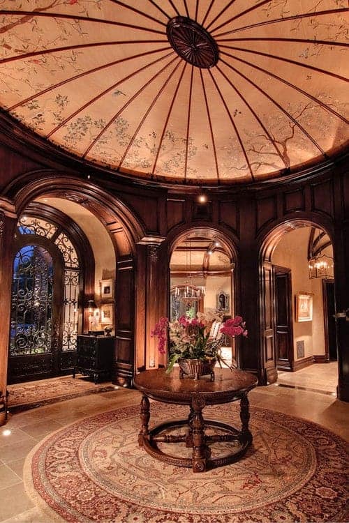 一个令人瞠目结舌的门厅，在装饰好的圆顶天花板下的圆形地毯上放着一张花式餐桌。