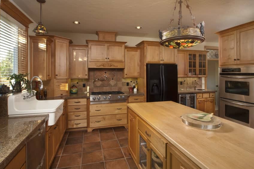 这间厨房拥有棕色橱柜、厨房柜台和中心岛，以及棕色瓷砖地板。